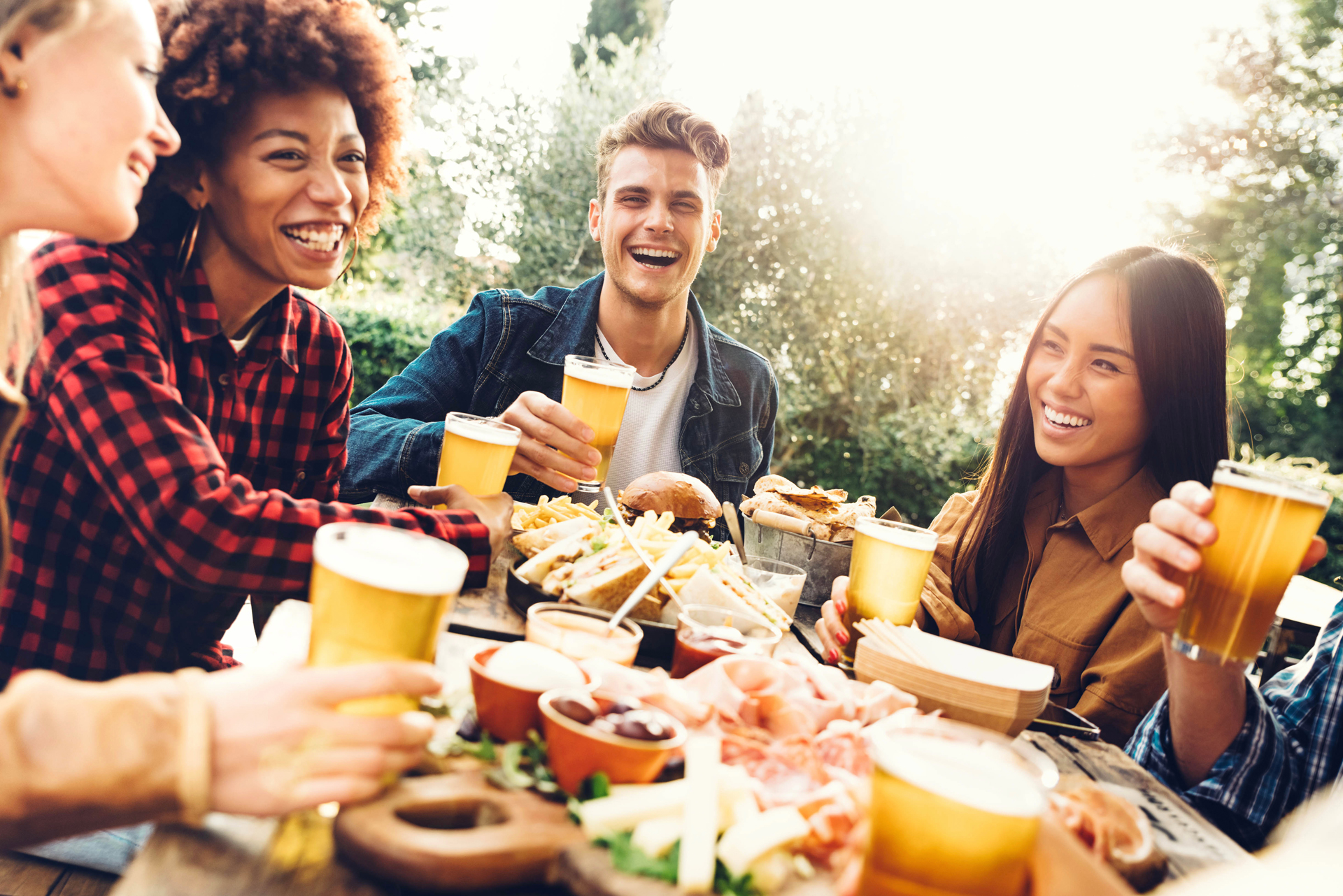 Fünf junge Menschen sitzten mit einer Brotzeit am Tisch und stoßen mit Bier an