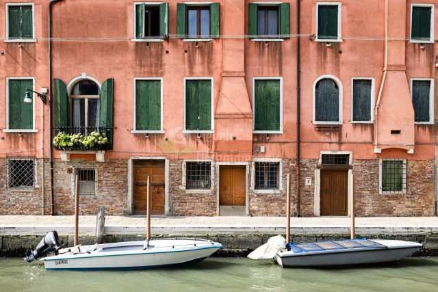 An orange house with 2 boats on some canal in Venice, Italy