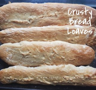 4 long crusty bread loaves laying stacked on a baking tray