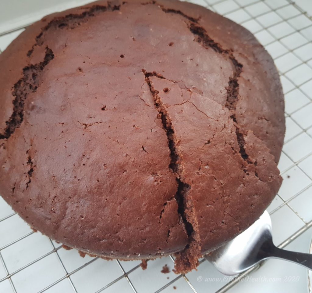 Whole chocolate cake on a wire rack with one slice cut on a silver cake slice.