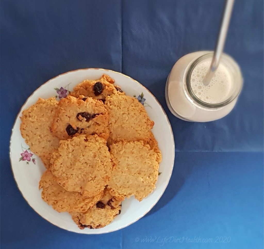 Plate of cookies with a bottle of milk and a stainless steel straw on a navy blue background.