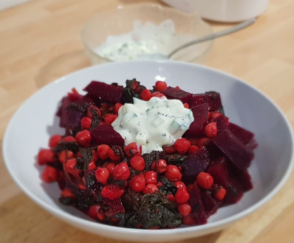 Beetroot, chickpea & spinach curry in a white bowl with raita on top