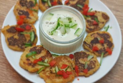 Plate of vegetable mash fritters on a white plate, with raita dip in centre