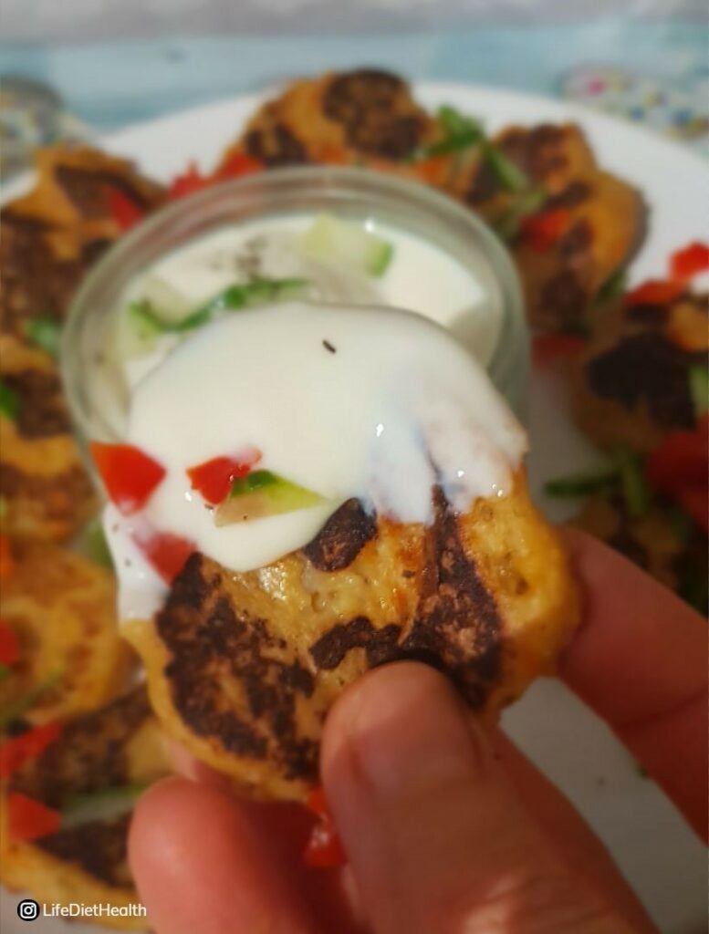 Close up fritter with yogurt dip. Plate of fritters in background.