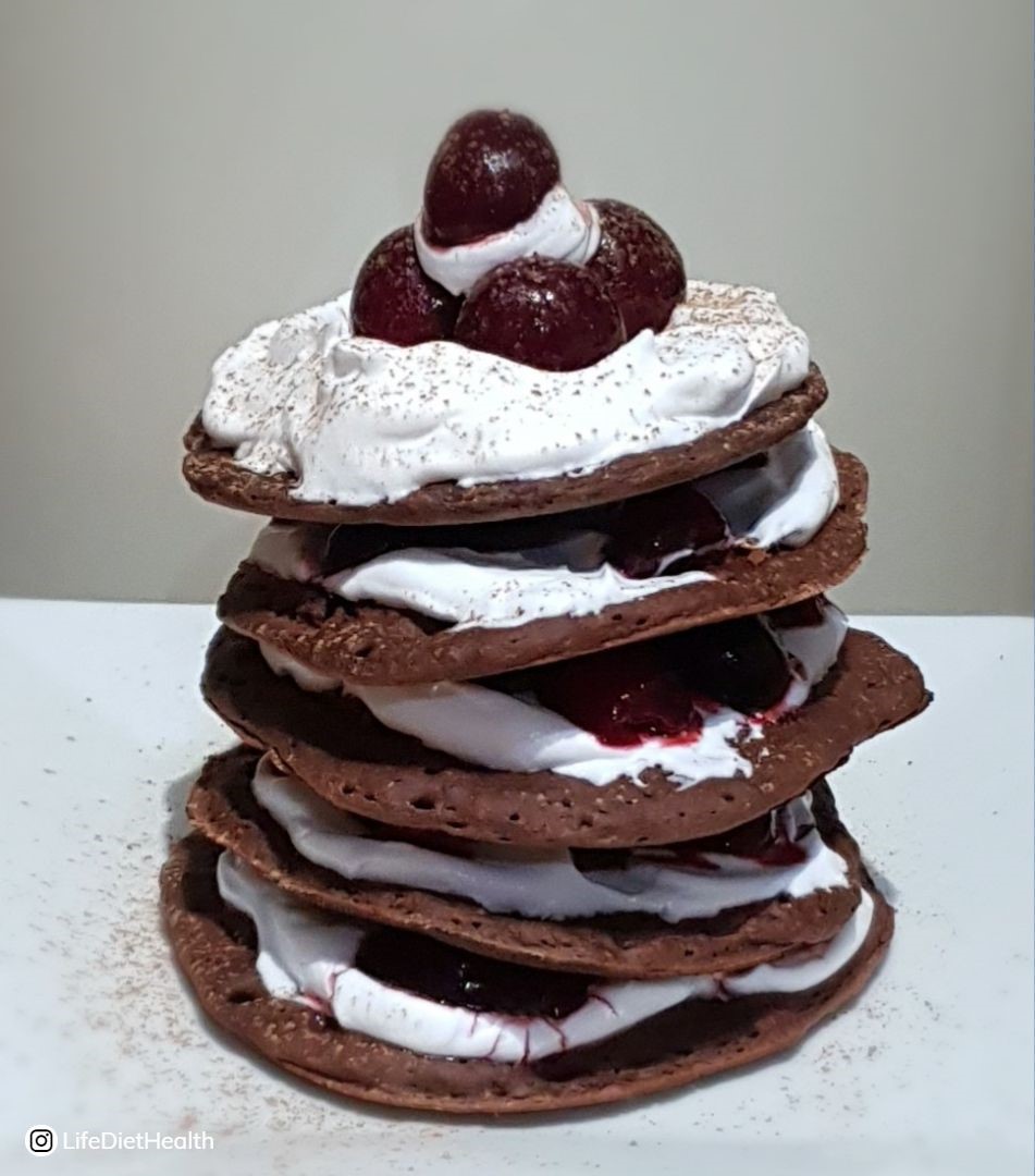 tall stack of chocolate pancakes with cherries and cream on a white plate