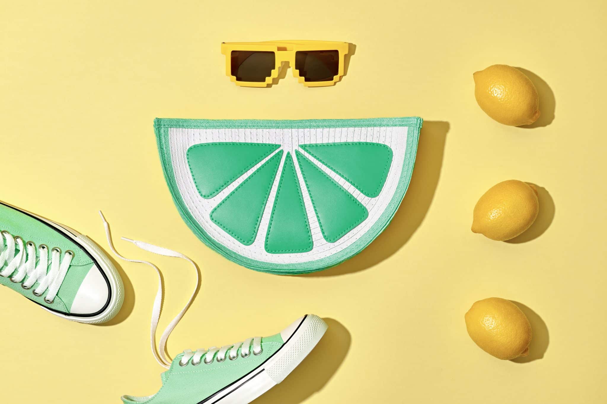 Image of green and white sneakers with one shoe untied, a green and white lemon slice-shaped purse, pixelated yellow sunglasses, and four lemons arranged on a yellow background. One shoe, the purse, and the sunglasses are arranged to resemble a face—an intriguing metaphor for personal development.