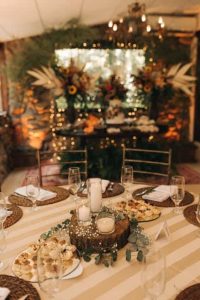 As a coach for women, I understand the importance of creating inviting spaces for meaningful gatherings. Picture a decorated round table with a striped tablecloth, elegant glassware, plates of appetizers, and candles arranged on a wooden centerpiece—perfect for fostering conversation and connection. In the background, large floral arrangements and warm ambient lighting set an inspiring scene ideal for women to relax, share experiences, and support one another. coach