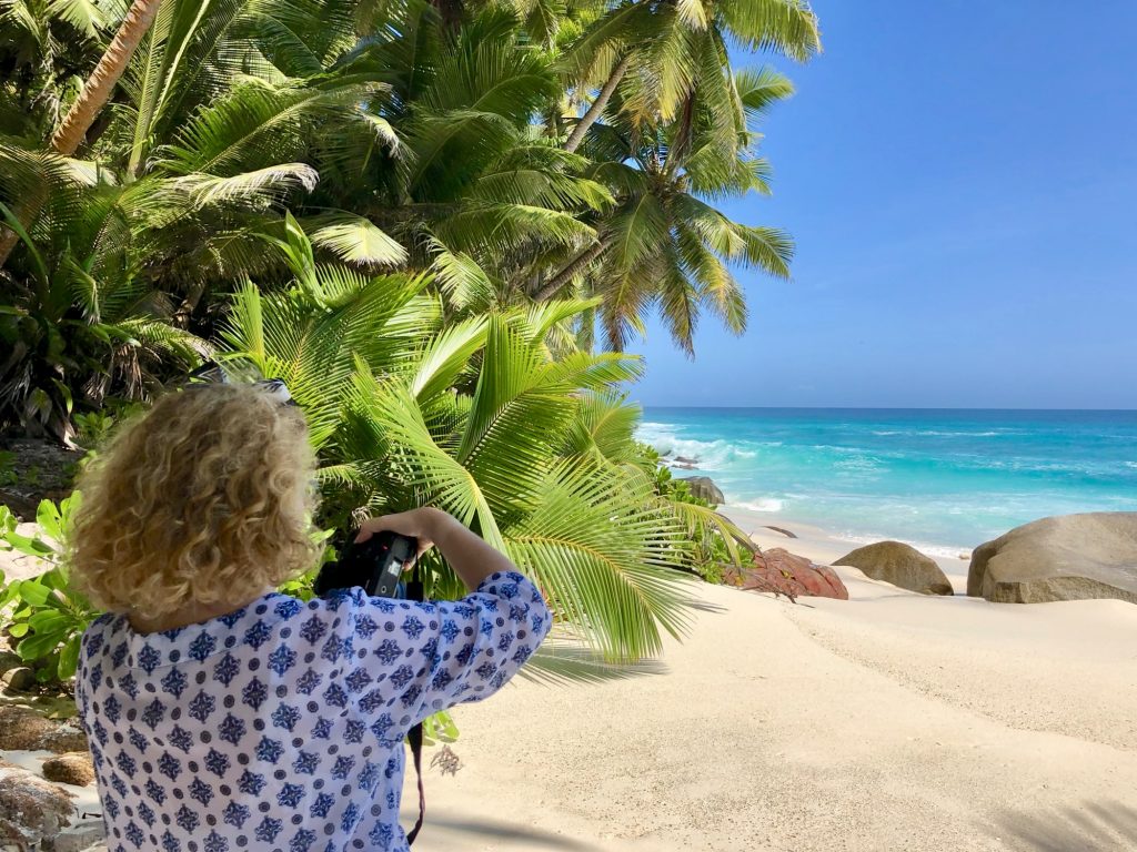 A blonde woman seen from her back and holding a camera at Anse Victorin beach on Fregate Island. Photo by Mihaela Limberea.