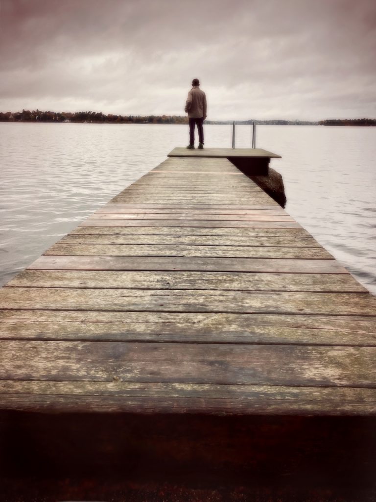 Dark mood photo of a man at the ned of a jetty. iPhone photo by Mihaela Limberea.