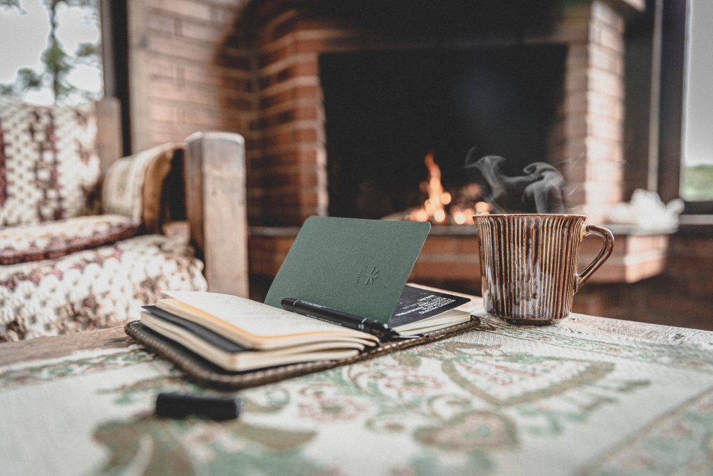 Coffee mug and notebook near a fireplace. 