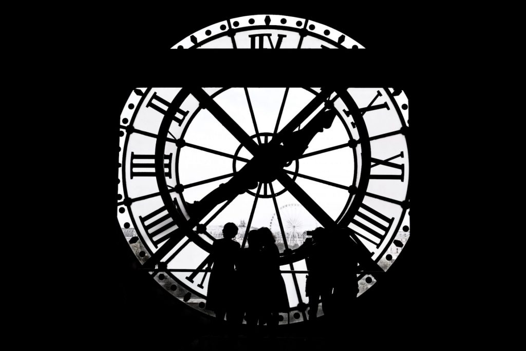 Black and white photo of a group of people standing in front of the clock at the Orsay Museum in Paris, France