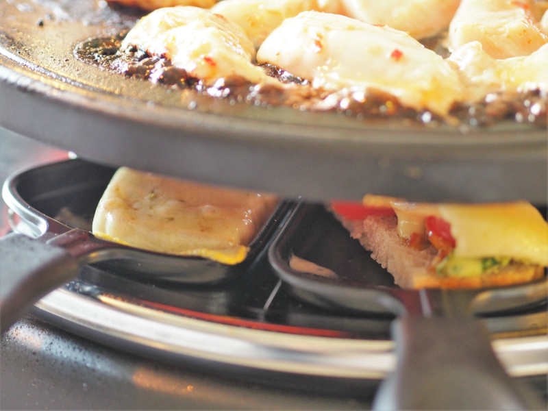 bilde av en raclette med skuffene fylt av loff, ost og tilbehør til et sosialt måltid