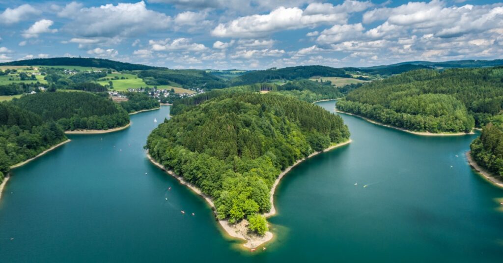 Teichlandschaft mit bewaldeten inseln und ufer, grünlandschaft im hintergrund, blauer himmel mit wolken, natur pur, Lindweiler.