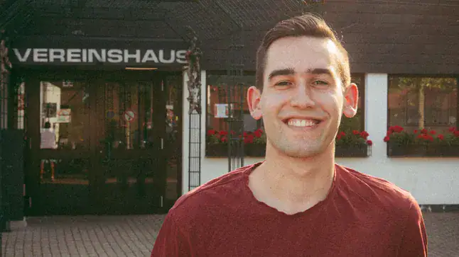 Mann lächelnder junger mann vor Vereinshaus in lindweiler, strahlende gesichtsausdruck, freundliche atmosphäre, outdoor foto, gesellschaftliches engagement.