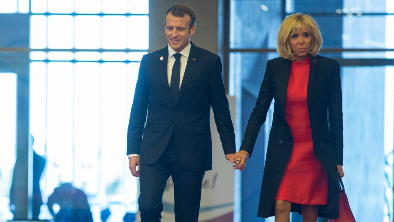 Junge Mann und ältere Frau halten Händchen, gehen zusammen durch ein modernes Gebäude, symbolisieren Zusammenarbeit und Vertrauen.