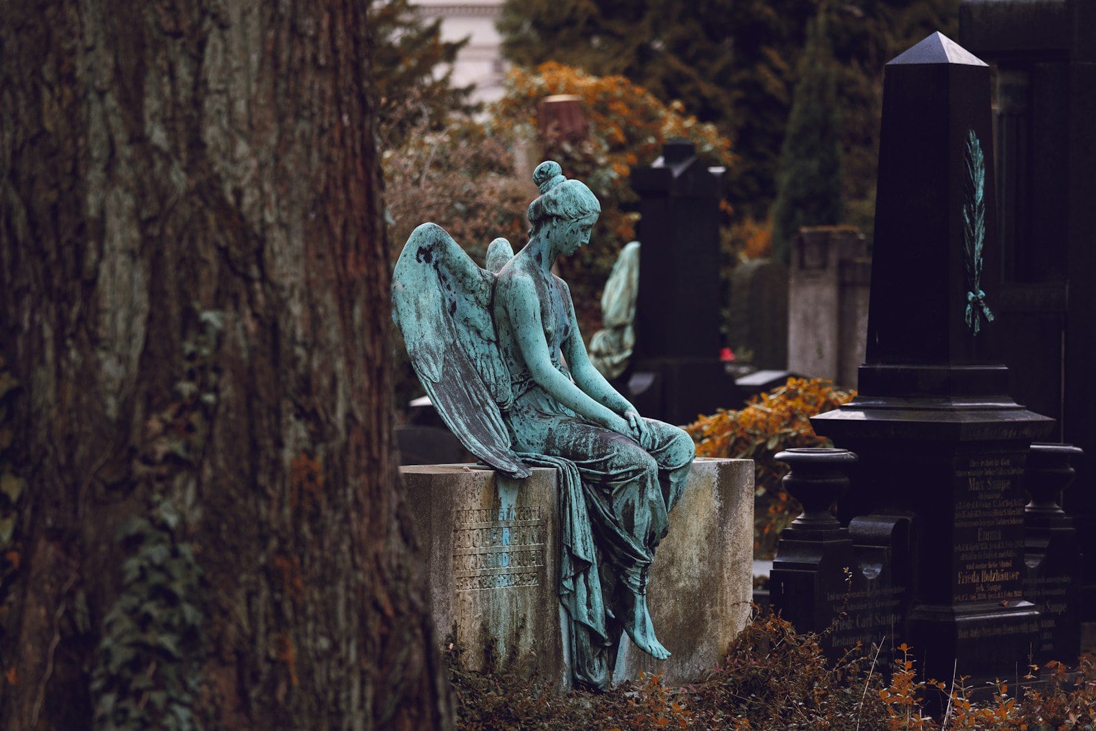 Feengestalt auf einem Grabstein in einem Friedhof mit Herbstlaub, emotionaler Friedhofszauber, künstlerische Skulptur in grün patiniertem Metall, Stillleben im verzauberten Friedwald.