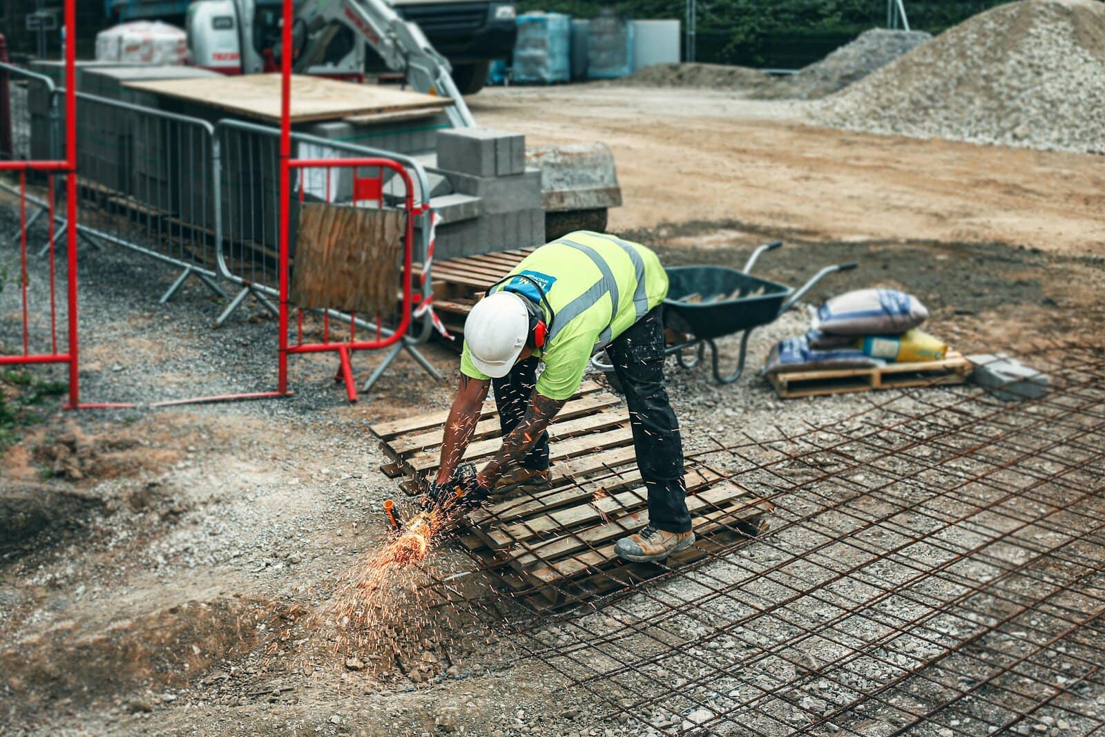 Bauarbeiter schweißt Stahlbewehrung auf einer Baustelle, in der Nähe von Baumaterialien und Werkzeugen, bei einer Baustellenarbeit.