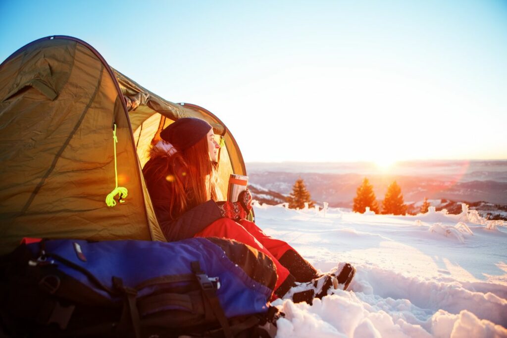 Kvinna sitter vid tält i vintersnön