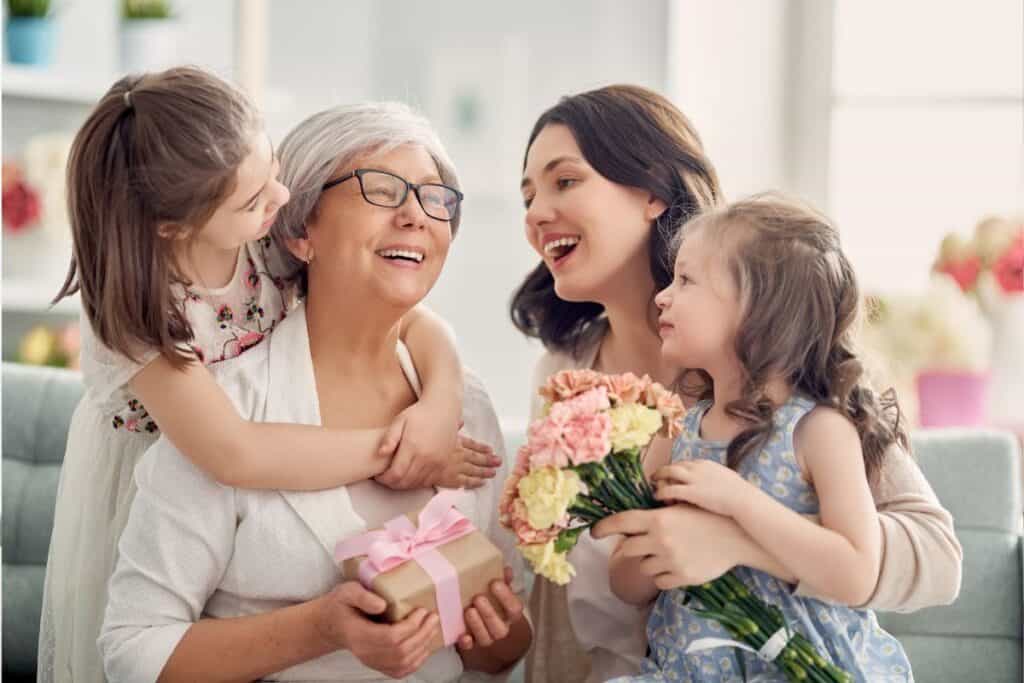 Mormor, mamma och två barnbarn på mors dag med blommor och paket