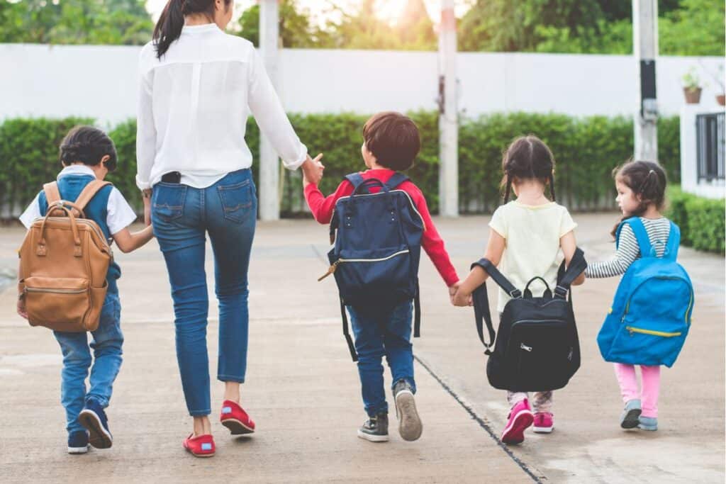 Mamma och fyra barn som är på väg till skolan håller varandra i handen