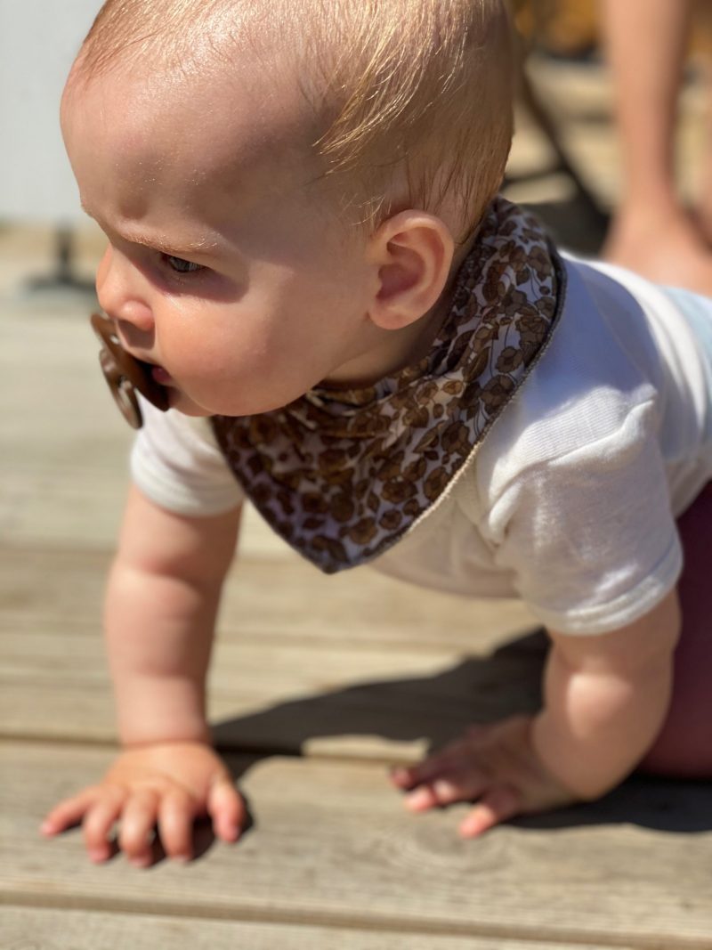 Baby med sut der kravler på træterrasse