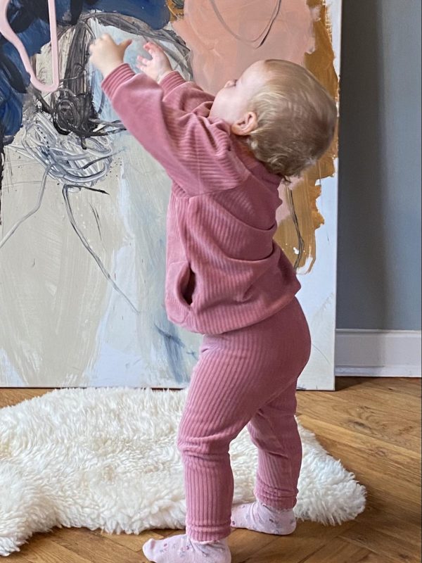 Baby der står i et lyserødt sæt tøj ved et lammeskind