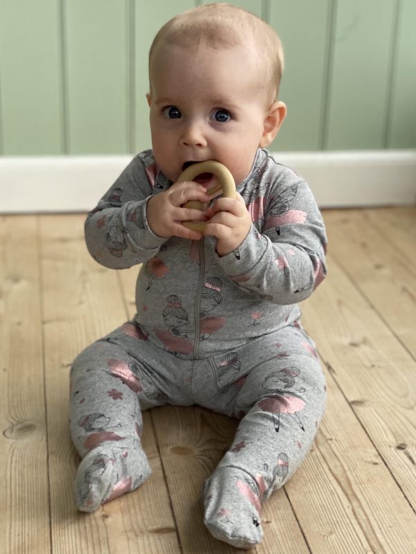 Baby med bidering på trægulv i grå heldragt