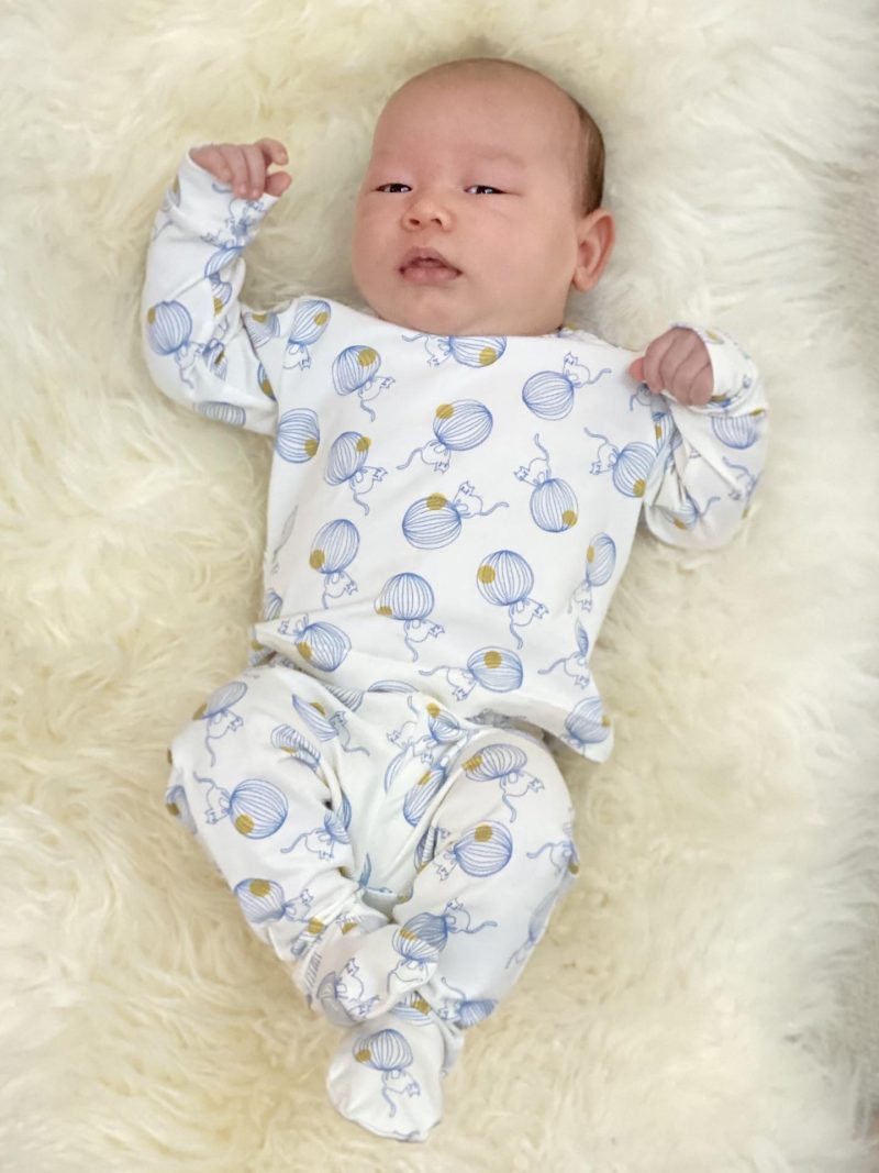 Baby der ligger på et lammeskind i hvid pyjamas med mønster