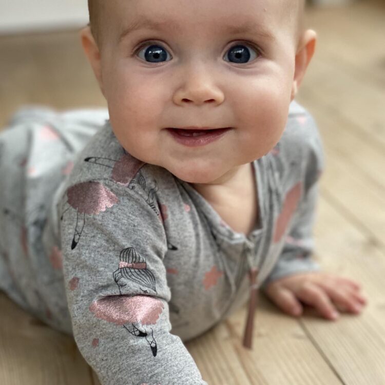 Baby iført pyjamas ligger på gulvet og smiler 
