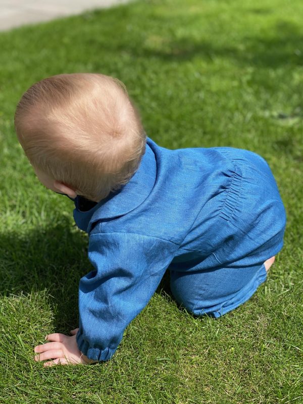 Baby der kravler på græsplæne i blå dragt