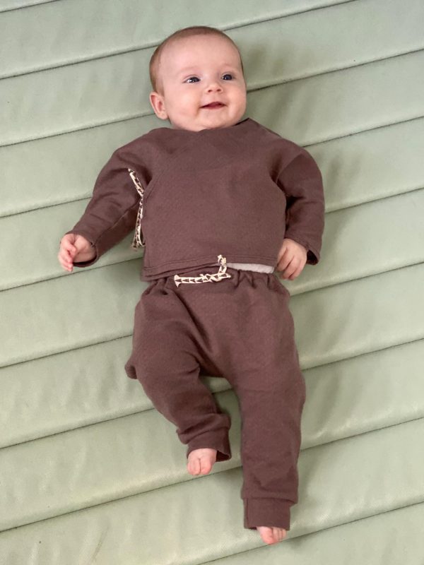 Baby in a brown suit with tied strings on a green gym mat