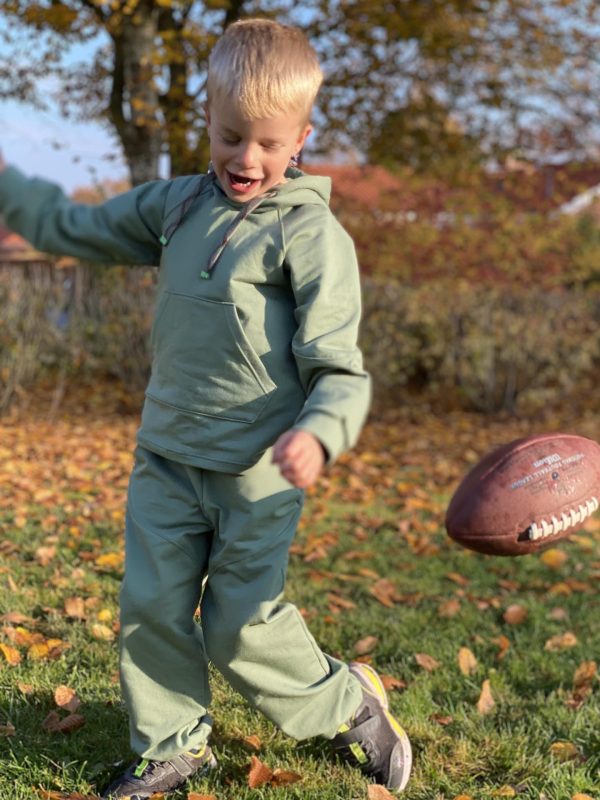 Boy playing in green jogging suit with a ball on a green field