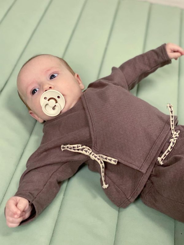 Baby in a brown jacket on a green gym mat