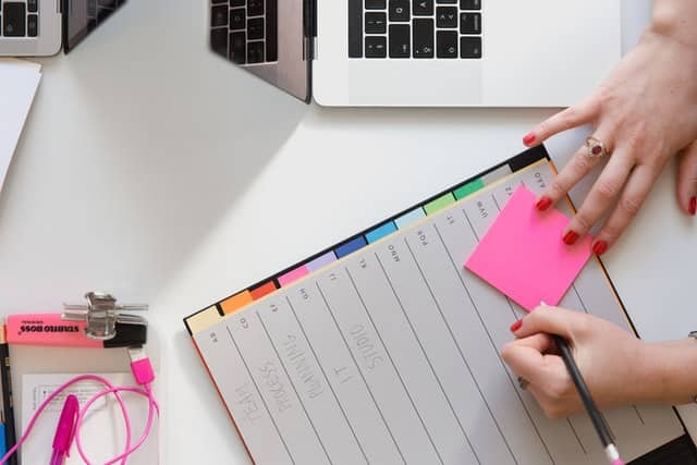 Picture showing a computer and a hand writing on a post-it note.
