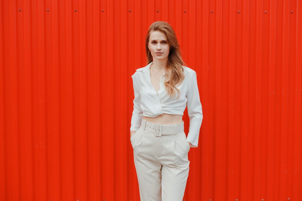 Elegant woman in white top and trousers walking with red metal wall in background