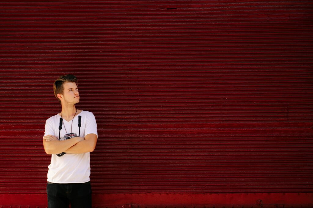 stylish hipster man posing on background of red garage door in sunny street