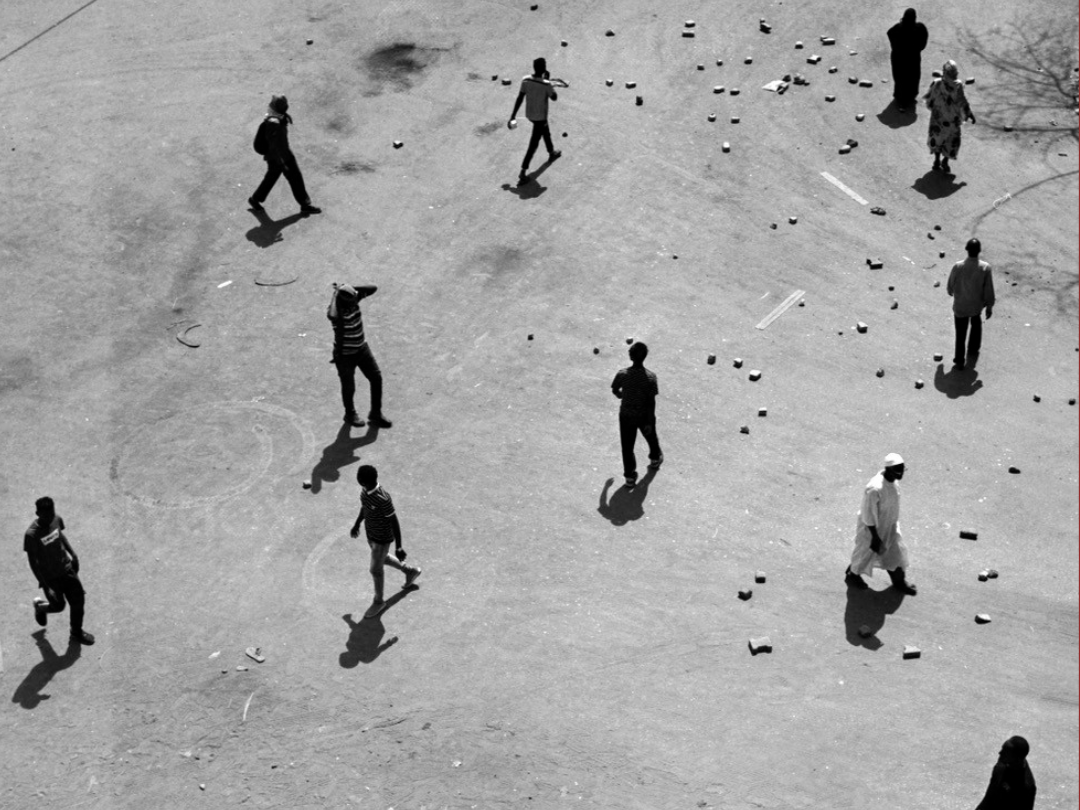 Black and white image of people walking across a wide stretch of earth taken from above © Ala Kheir, Khartoum, Sudan, 2023 
