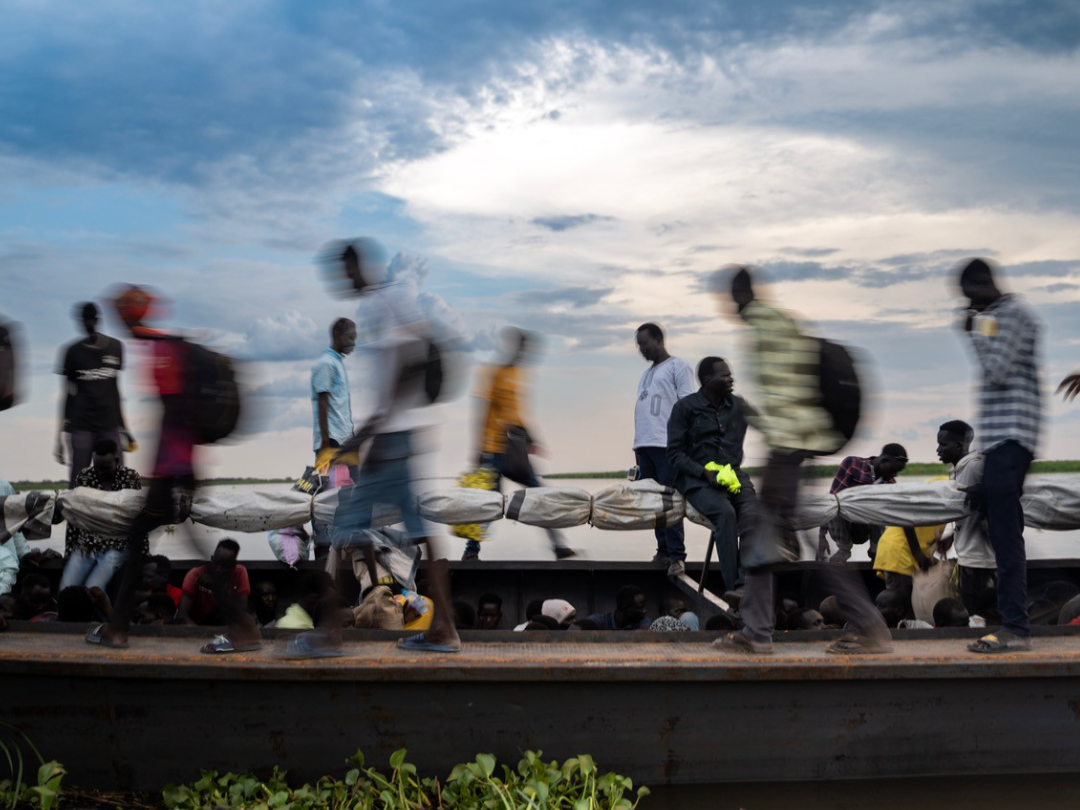 Blurred people walk across a raised sidewalk against a blue sky © Ala Kheir, Wad Medani, Sudan, 2023 
