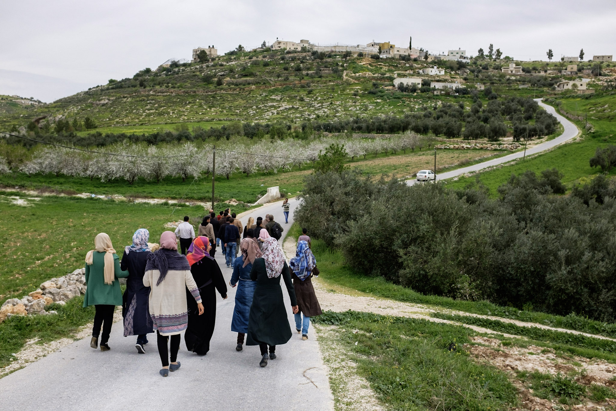 group of women in hijabs walking away on a road towards village