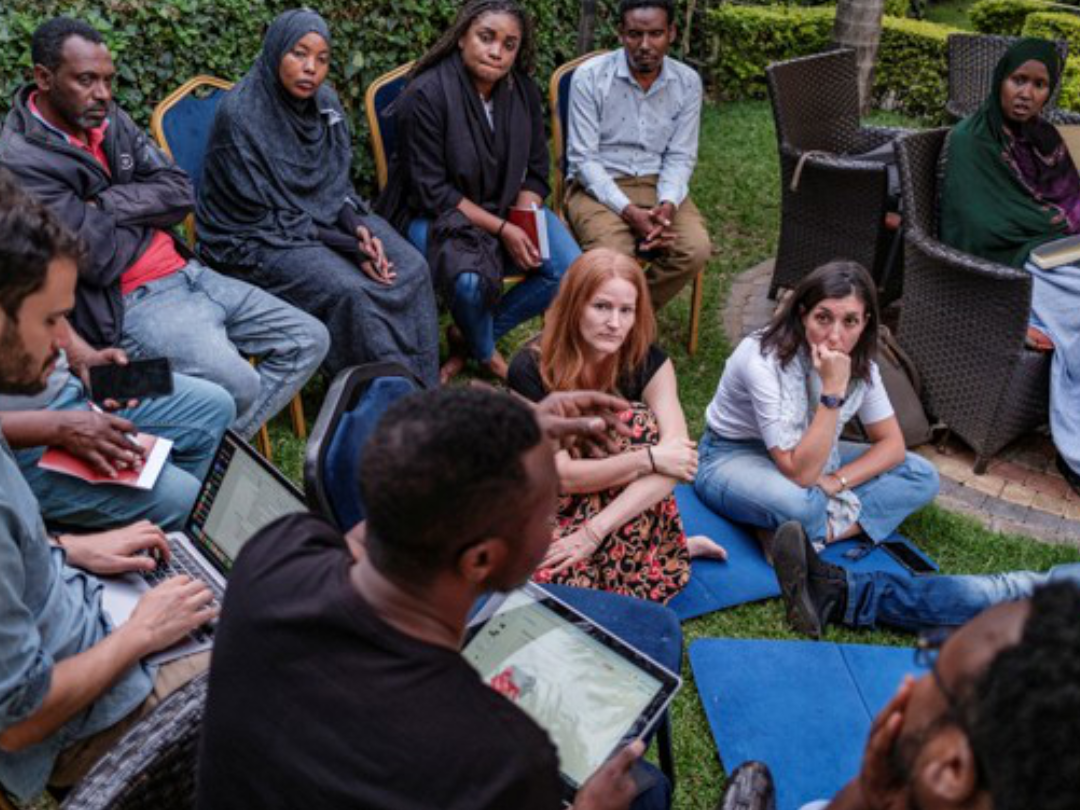 a group of people sit in a circle some on chairs some on the ground talking
