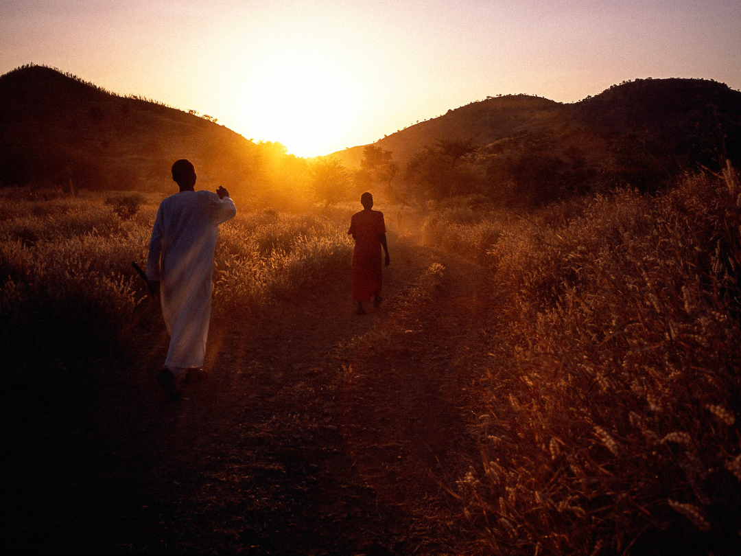 Sunset two people walk into the sunset away from camera (Nuba Mountains, Sudan)