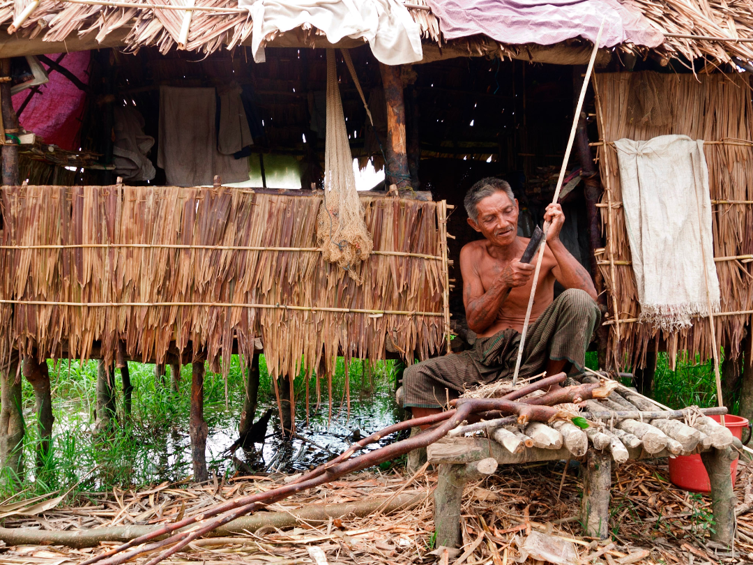 man cutting sticks An elderly Myanmar man whittles sticks in front of a reed house (Irrawaddy Delta)