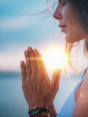 Young woman meditating with her eyes closed, practicing Yoga with hands in prayer position.