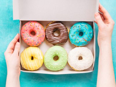 Top view of female hands holding box with colorful donuts on blue concrete background