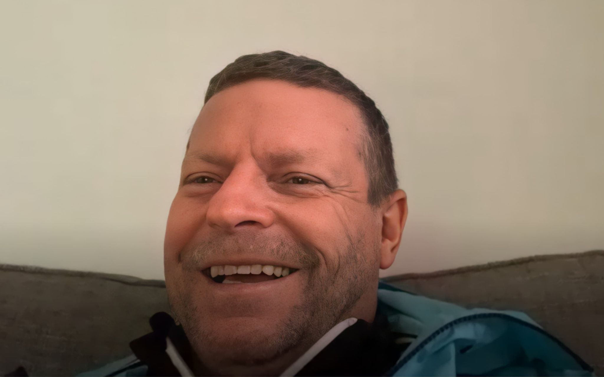 Micky Hazard, former Tottenham Hotspur player, talking about his efforts to stop loneliness over lockdown. He is wearing a blue windbreaker jacket, sitting in his living room, and smiling. 