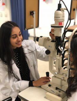 Shaan Bhachu, a student optometrist, in a white lab coat using equipment to examine the eyes.