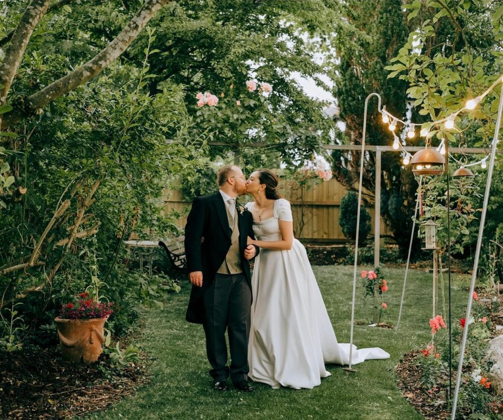 Adriana and Lewis stand hand in hand, gazing lovingly into each other's eyes on their wedding day in Penarth, surrounded by the beauty of the seaside town and the warmth of their friends and family.