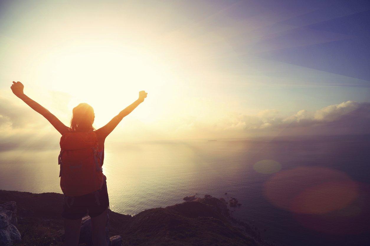 cheering young woman backpacker at sunrise seaside mountain peak