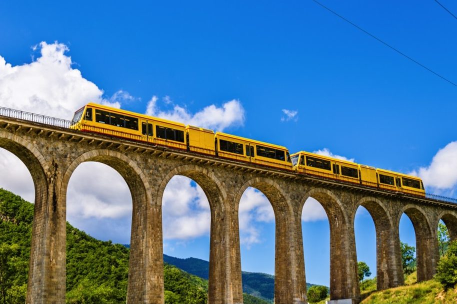 Gele trein rijdt over een spoorwegviaduct in de Pyreneeën.