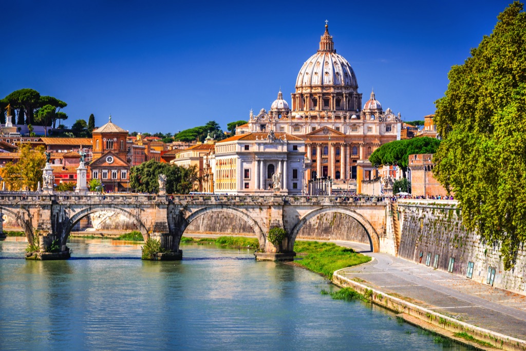 Zicht op de rivier Tiber in Rome, met een brug en de Sint-Pietersbasiliek op de achtergrond.